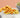 Mixed variety of crunchy snacks and a bowl of roasted green peas on a white table with peach background